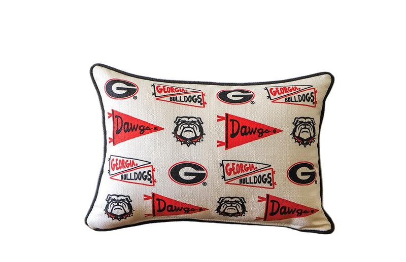 Decorative pillow with Georgia Bulldogs logos on a wooden surface against a white wall.
